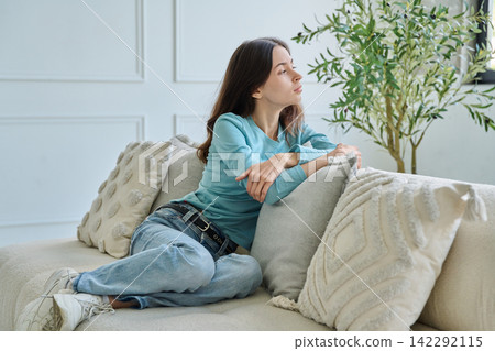 Pensive teen student girl sitting thoughtful on sofa leaning hand Pensive teen student girl sitting thoughtful on sofa leaning hand 142292115