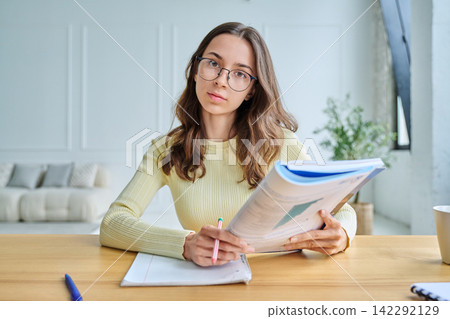 Young female student sitting at desk holding textbook webcam view Young female student sitting at desk holding textbook webcam view 142292129
