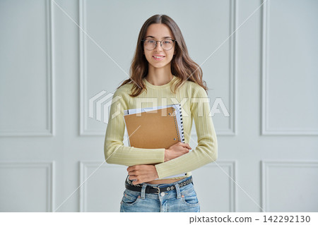 Portrait of young female college student holding notebooks against wall Portrait of young female college student holding notebooks against wall 142292130