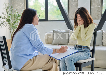 Upset young woman covering face during therapy session with psychologist Upset young woman covering face during therapy session with psychologist 142292133