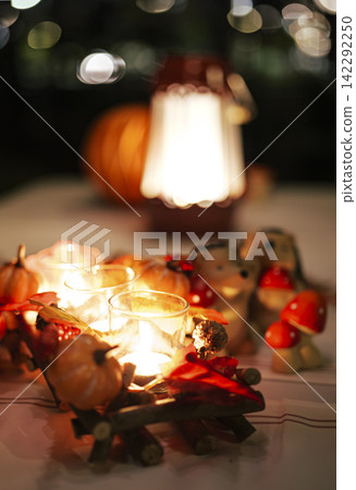 Glowing decorative candles and red metal lantern on a table at night illustrate a warm seasonal centerpiece for festive evenings. Glowing decorative candles and red metal lantern on a table at night illustrate a warm seasonal centerpiece for festive evenings. 142292250