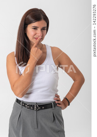 Young woman pinching her nose and frowning at a bad smell, holding her breath and looking away in a studio portrait against a white background, showing clear discomfort Young woman pinching her nose and frowning at a bad smell, holding her breath and looking away in a studio portrait against a white background, showing clear discomfort 142293276