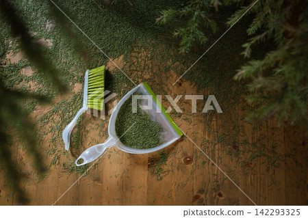 Sweeping fallen Christmas tree needles with brush and dustpan Sweeping fallen Christmas tree needles with brush and dustpan 142293325