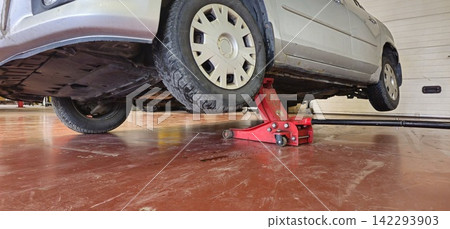 Red jack supports silver car in garage Red jack supports silver car in garage 142293903
