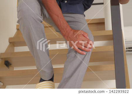 A senior man appears to be in pain in his knees while going up and down the stairs. A senior man appears to be in pain in his knees while going up and down the stairs. 142293922