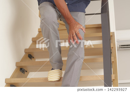 一位老年男子上下樓梯時似乎膝蓋疼痛。 一位老年男子上下樓梯時似乎膝蓋疼痛。 142293927