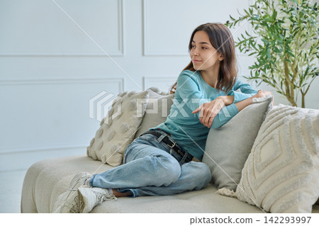 Relaxed young woman sitting comfortably on couch looking away smiling Relaxed young woman sitting comfortably on couch looking away smiling 142293997