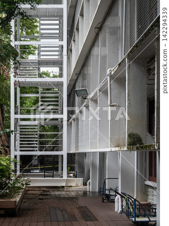 A compelling architectural perspective highlighting the stark geometric lines of an external industrial steel staircase adjacent to a textured concrete facade. A compelling architectural perspective highlighting the stark geometric lines of an external industrial steel staircase adjacent to a textured concrete facade. 142294339