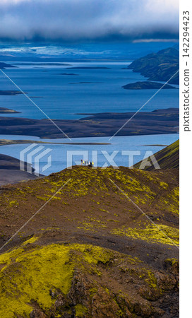 Aerial view of moss-covered volcanic terrain with hikers overlooking glacial lakes, Iceland Aerial view of moss-covered volcanic terrain with hikers overlooking glacial lakes, Iceland 142294423