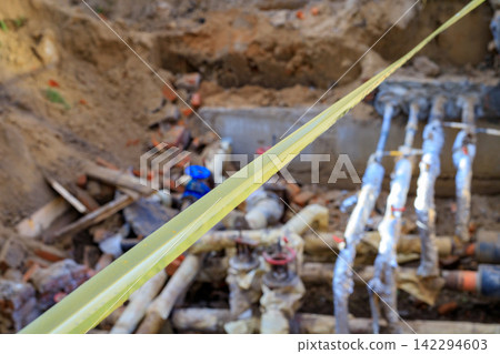Yellow Warning Tape Across Excavated Trench for Underground Pipeline and Infrastructure Repair 142294603