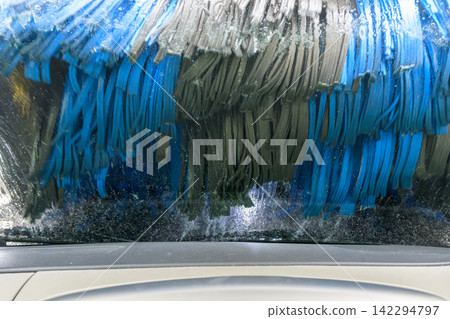 The blue brushes of an automatic car wash machine washing the windshield (from inside the car). The blue brushes of an automatic car wash machine washing the windshield (from inside the car). 142294797