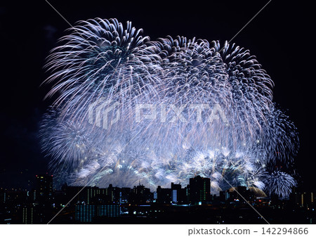 淡藍色的煙火在夜空中綻放,與城市夜景的燈光交相輝映。 淡藍色的煙火在夜空中綻放,與城市夜景的燈光交相輝映。 142294866