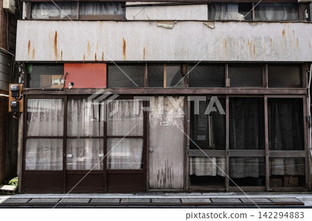 The red rust streaks running down the exterior wall tell a story of history: the facade of an old shop and residence with a Showa-era retro feel. The red rust streaks running down the exterior wall tell a story of history: the facade of an old shop and residence with a Showa-era retro feel. 142294883