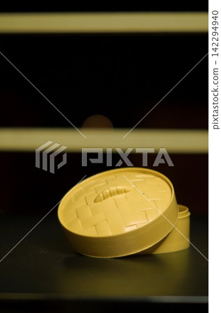Open round yellow container with its lid tilted beside it is isolated on a dark tabletop. The image represents access, storage, simplicity, and readiness to reveal hidden contents Open round yellow container with its lid tilted beside it is isolated on a dark tabletop. The image represents access, storage, simplicity, and readiness to reveal hidden contents 142294940