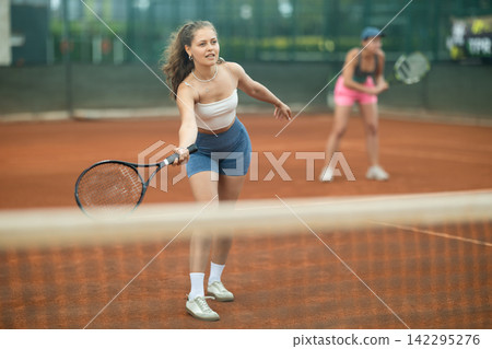 Sporty young girl playing doubles tennis on outdoor court 142295276