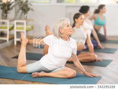 Elderly woman doing one legged king pigeon pose during yoga training Elderly woman doing one legged king pigeon pose during yoga training 142295289