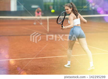 Young female tennis player engrossed in game on clay court Young female tennis player engrossed in game on clay court 142295299