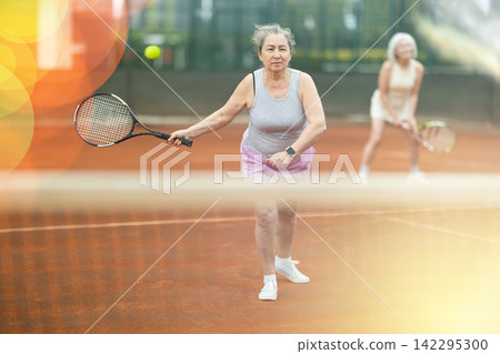 Senior woman playing doubles tennis on outdoor court Senior woman playing doubles tennis on outdoor court 142295300