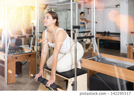 Young woman making pilates exercising while standing on knees using Wanda chair machine Young woman making pilates exercising while standing on knees using Wanda chair machine 142295317