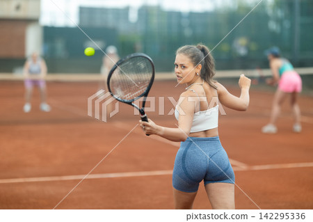 Young female tennis player engrossed in doubles on clay court Young female tennis player engrossed in doubles on clay court 142295336