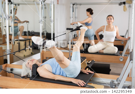 Senior woman doing stretching exercises on pilates reformer Senior woman doing stretching exercises on pilates reformer 142295349