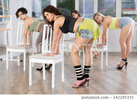 Group of women in high heels rehearsing dance while leaning on chair Group of women in high heels rehearsing dance while leaning on chair 142295355