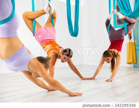 Group of women doing bow pose in suspended hammocks with palms on floor 142295356