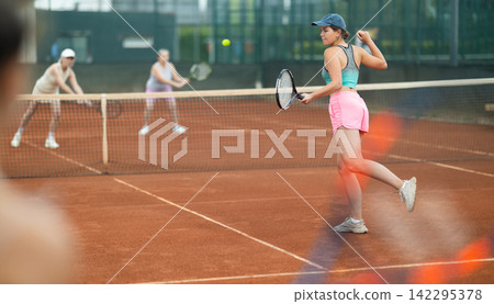 Young female tennis player engrossed in doubles on clay court Young female tennis player engrossed in doubles on clay court 142295378