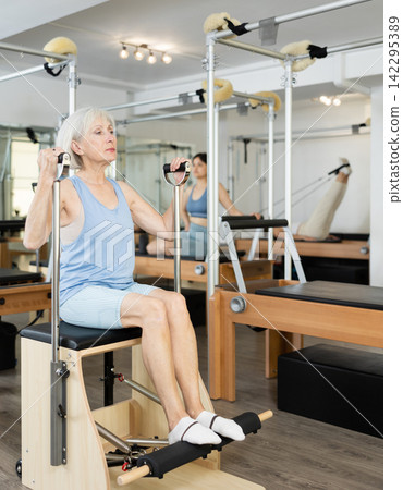Senior woman doing exercises on wunda chair in pilates studio Senior woman doing exercises on wunda chair in pilates studio 142295389