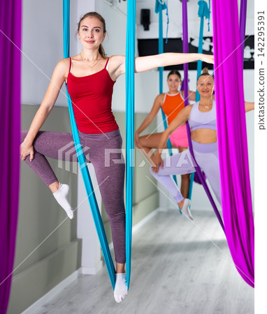 Sporty young woman doing aerial yoga asanas with suspended hammock Sporty young woman doing aerial yoga asanas with suspended hammock 142295391