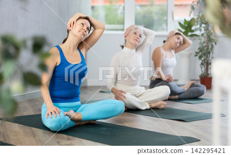 Group of sporty woman practicing yoga pose Gomukhasana in yoga studio Group of sporty woman practicing yoga pose Gomukhasana in yoga studio 142295421