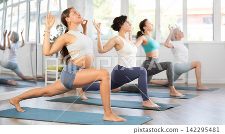 Woman performing revolved side angle pose Parivrtta Parsvakonasana during yoga class with female group in fitness studio Woman performing revolved side angle pose Parivrtta Parsvakonasana during yoga class with female group in fitness studio 142295481