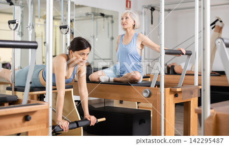 Focused woman performing set of pilates exercises on reformer in fitness studio. Healthy active lifestyle concept Focused woman performing set of pilates exercises on reformer in fitness studio. Healthy active lifestyle concept 142295487