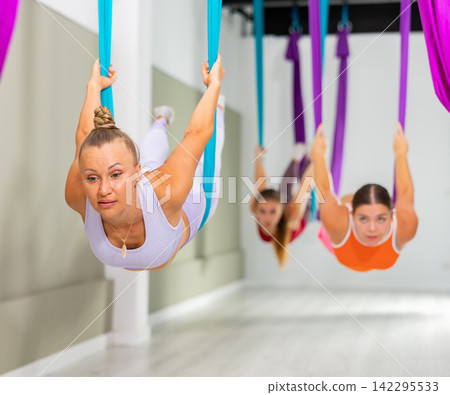Woman performing Salabhasana asana in hanging hammock during aerial yoga training Woman performing Salabhasana asana in hanging hammock during aerial yoga training 142295533