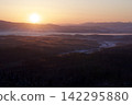 The rising sun and morning mist flowing through the snowy valley. 142295880
