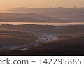 A snow-covered rural village and winter mountain range bathed in soft light. 142295885