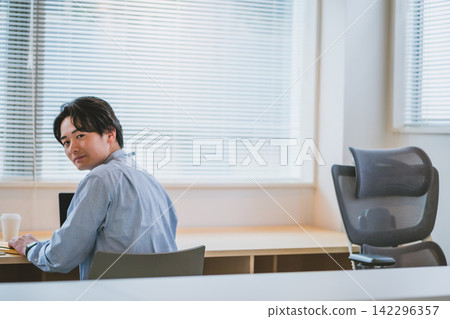 An office scene featuring a male business person turning around at his desk and smiling. An office scene featuring a male business person turning around at his desk and smiling. 142296357