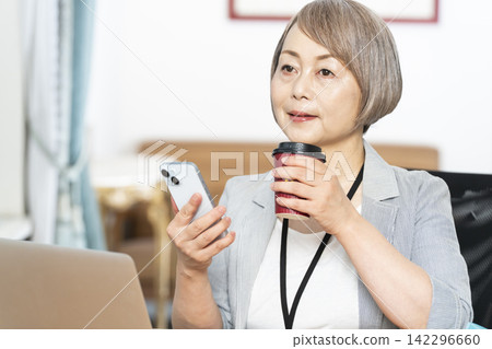 Senior woman drinking coffee while working in the office Senior woman drinking coffee while working in the office 142296660