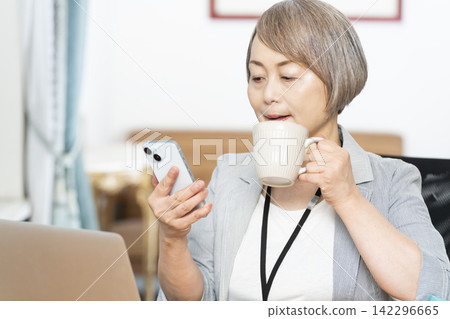 Senior woman drinking coffee while working in the office Senior woman drinking coffee while working in the office 142296665