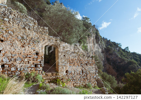 View of ancient Afkule monastery carved into high vertical cliffs near Oludeniz, Turkey. Dramatic rock landscape and historic architecture. Travel, cultural destination. 142297127