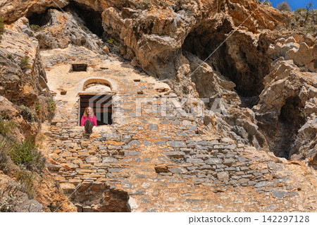 Woman looking at beautiful view from window of Afkule monastery carved into high vertical cliffs near Oludeniz, Turkey. Dramatic rock landscape and historic architecture. Travel, cultural destination. 142297128