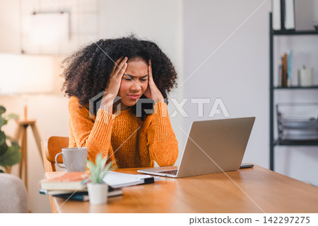 African American woman holding her forehead in frustration while working on a laptop, showcasing stress and exhaustion. African American woman holding her forehead in frustration while working on a laptop, showcasing stress and exhaustion. 142297275