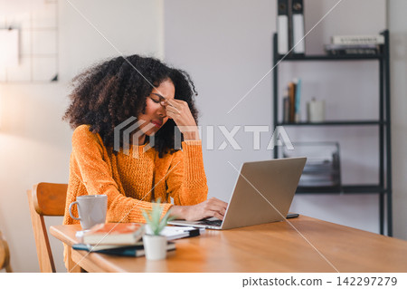 African American woman holding her forehead in frustration while working on a laptop, showcasing stress and exhaustion. 142297279