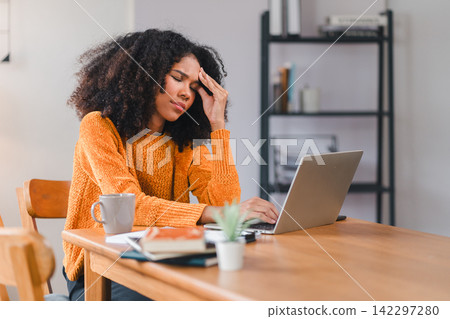 African American woman holding her forehead in frustration while working on a laptop, showcasing stress and exhaustion. African American woman holding her forehead in frustration while working on a laptop, showcasing stress and exhaustion. 142297280