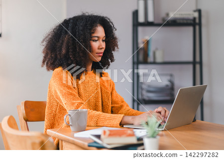 Smiling African American woman using a laptop while working from home. Smiling African American woman using a laptop while working from home. 142297282