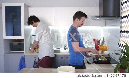 The home life of two young gay men. A man cooks dinner for his boyfriend in the kitchen. The friends met in the shared kitchen The home life of two young gay men. A man cooks dinner for his boyfriend in the kitchen. The friends met in the shared kitchen 142297476