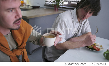 A couple of students are chatting over breakfast. Two men are sitting at a table, one is drinking coffee, and the other is finishing his lunch A couple of students are chatting over breakfast. Two men are sitting at a table, one is drinking coffee, and the other is finishing his lunch 142297501