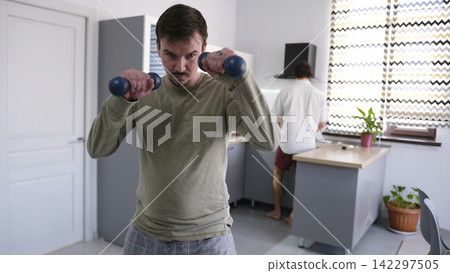 A man is working out in the living room. The guy is engaged in boxing. A gay man lifts dumbbells against the background of a stylish kitchen A man is working out in the living room. The guy is engaged in boxing. A gay man lifts dumbbells against the background of a stylish kitchen 142297505
