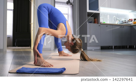 The peace and tranquility of yoga classes. A young female yogi stands in an asana. She's doing Pilates in her living room The peace and tranquility of yoga classes. A young female yogi stands in an asana. She's doing Pilates in her living room 142297641