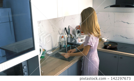 The household cares of a loving housewife. A woman washes dirty dishes after lunch in the kitchen 142297673